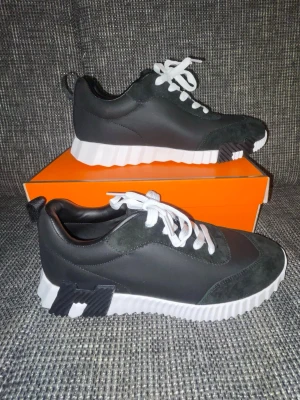 Svarta H sneakers med vit sula - Snygga svarta sneakers med vit, räfflad platåsula och vita skosnören. Skorna har detaljer i mocka och läderimitation samt coola svarta och vita inslag på sulan. Perfekta för dig som vill sticka ut med en modern och trendig look.