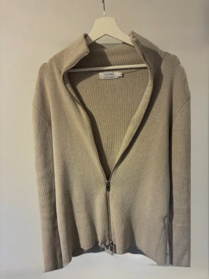 Beige ribbad ziptröja från LUNG - Säljer en beige ribbad tröja från LJUNG med dragkedja framtill och hög krage. Tröjan har långa ärmar och är tillverkad i ett mjukt, stretchigt material. Har ni frågor så är det bara o skriva. 