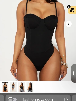 Svart body med bygel från Fashion Nova - Snygg svart body med bygelkupor och smala axelband från Fashion Nova. Figurnära passform och hög benskärning ger en modern siluett. Perfekt att styla med kjol eller jeans. Materialet är stretchigt och bekvämt.