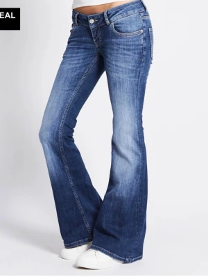 Blå bootcut jeans med utsvängda ben - Säljer ett par klassiska blå bootcut jeans med utsvängda ben och normalhög midja. Jeansen har fem fickor, knappgylf och snygga slitningar för en trendig look. Perfekta för dig som gillar retrostil och vill ha ett par bekväma jeans i bomull.