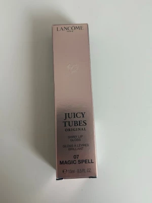 Lancôme Juicy Tubes Magic Spell - Lancôme Juicy Tubes Original i nyansen 07 Magic Spell är ett glansigt läppglans i tub med skimrande rosa färg. Förpackningen är elegant och genomskinlig med guldtext, och innehåller 15 ml. Perfekt för dig som vill ha glansiga och fylliga läppar med en hint av rosa.