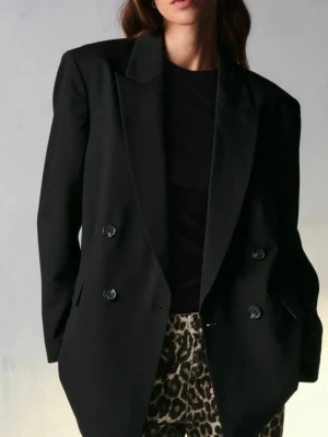 Svart oversized dubbelknäppt kavaj - Stilren svart oversized kavaj med dubbelknäppning och breda slag. Fyra knappar vid ärmslut och två fickor framtill. Klassisk modell som ger en cool och trendig look. Materialet ser ut att vara en mjuk ullblandning. Den är använd bar två gånger. 