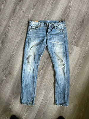 Ljusblå slitna jeans med raka ben - Säljer ett par ljusblå jeans med slitningar och distressed detaljer på både fram- och baksida. Jeansen har raka ben, klassisk femficksmodell och är tillverkade i denim. Perfekta för en avslappnad och trendig look.