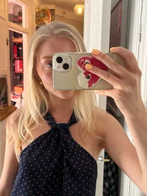 Mörkblå prickig halterneck topp - Säljer en mörkblå halterneck topp med små vita prickar. Toppen har en lös passform och är ärmlös, perfekt för varma dagar eller somrig stil. Tyget känns lätt och luftigt.