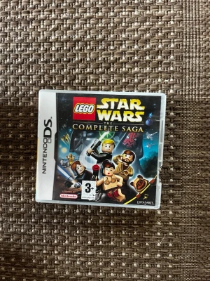 LEGO Star Wars The Complete Saga DS - LEGO Star Wars: The Complete Saga till Nintendo DS. Omslaget har färgglada LEGO-figurer från Star Wars-universumet och spelet är märkt för åldrar 3+. Perfekt för dig som gillar action, äventyr och klassiska Star Wars-karaktärer i LEGO-format.