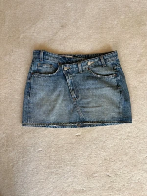  jeanskjol  - Säljer en klassisk blå jeanskjol med fem fickor och bälteshällor. Kjolen har en rak passform och stängs med knapp och dragkedja framtill. Perfekt till vardags för en avslappnad och trendig look.