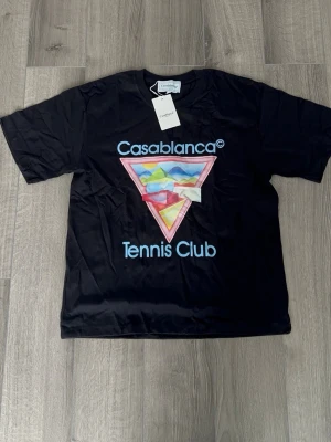 Svart Casablanca Tennis Club t-shirt - Svart t-shirt från Casablanca med färgglatt triangulärt tryck och texten 'Casablanca Tennis Club' på bröstet. Klassisk passform och rund hals. Tillverkad i mjuk bomull som känns skön mot huden. Perfekt för dig som gillar streetwear och grafiska prints.