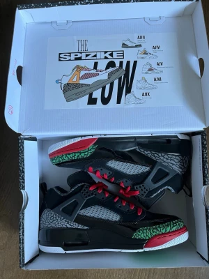 Jordan Spizike Low svart/röd/grön - Snygga Jordan Spizike Low sneakers i svart med röda och gröna detaljer samt grått elefantmönster. Skorna har meshpaneler på sidorna, röda skosnören och en vit sula med färgade inslag. Perfekt för dig som gillar unika och sportiga sneakers med streetwear-vibe.