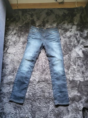 Jack & Jones jeans  - Snygga blå jeans från Jack & Jones med klassisk femficksmodell och raka ben. Jeansen har en knappgylf och är gjorda i bomull med lite stretch för extra komfort. Perfekta till vardagslooken och passar till det mesta i garderoben.