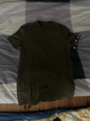 Olivgrön t-shirt från Dsquared2 - Snygg olivgrön t-shirt från Dsquared2 med rund hals och korta ärmar. På ena ärmen finns en svart detalj med texten 'ICONIC' i vitt. Tillverkad i mjuk bomull för skön känsla och stilren look.
