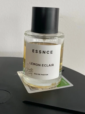 ESSNCE Lemon Eclair Eau de Parfum - Fräsch parfym från ESSNCE med doften Lemon Eclair. Kommer i en stilren, rund glasflaska med svart lock och vit etikett. Parfymen har en ljusgul vätska och modern design som passar perfekt för dig som gillar citrusdofter. Limited edition. Mängd enl bilderna