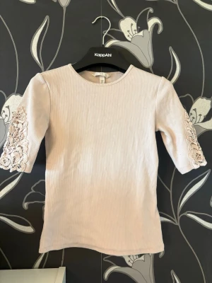 Ljusrosa topp med spetsärmar  Hm - Supersöt topp från Hm med ribbad struktur och trekvartsärmar. Ärmarna har fina spetsdetaljer som ger en romantisk vibe. Perfekt att styla med jeans eller kjol för en trendig look.