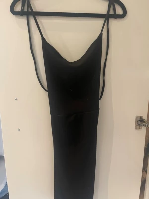 Svart långklänning med snörning - Säljer en svart långklänning med tunna axelband och snygg snörning i ryggen. Klänningen har en smickrande passform och är perfekt för dig som gillar en stilren och elegant look. Materialet känns mjukt och följsamt mot kroppen.