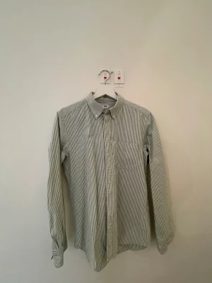 Grönvit randig skjorta Uniqlo Slim Fit - Säljer en grön- och vitrandig skjorta från Uniqlo i modellen Slim Fit. Skjortan har klassisk krage, långa ärmar och knäppning framtill. Tillverkad i mjuk bomull och passar perfekt för en clean och stilren look.