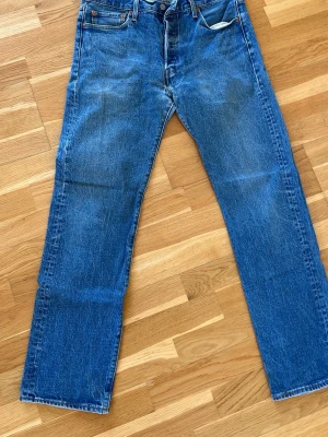 Levi's raka blå jeans - Klassiska blå jeans från Levi's med rak passform och fem fickor. Jeansen har en tidlös tvätt och är tillverkade i slitstark denim. Perfekta för en avslappnad och stilren look. BYXAN HAR HÅL.