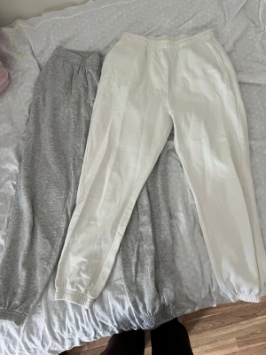 Mjukisbyxor Gina Tricot, vit & grå - Två par mjukisbyxor från Gina Tricot i färgerna vit och ljusgrå. Båda har resår i midjan och vid bensluten för en skön passform. Tillverkade i mjuk bomull från good collection, perfekt för chill dagar hemma eller när du vill vara bekväm. Säljes som ett par för 200kr eller singular 125kr.