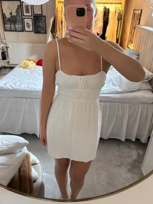 Vit kort sommarklänning med smala band - Söt vit kort klänning med smala axelband och lätt rynkad midja. Klänningen har en enkel, stilren design och är perfekt för varma dagar. Tillverkad i ett mjukt och luftigt material som känns bekvämt mot huden. Säljer pågrund av att den aldrig kommer till användning🤍