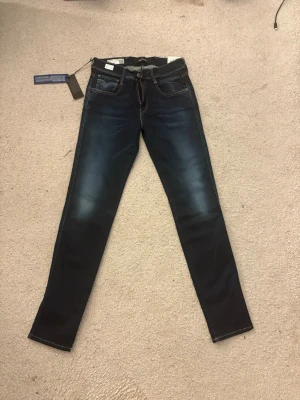 Mörkblå slim fit jeans från Replay - Snygga mörkblå slim fit jeans från Replay med klassisk femficksdesign och kontrastsömmar. Jeansen har en lätt tvättad look framtill och bakfickor med dekorativa sömmar. Tillverkade i stretchigt denim för extra komfort.