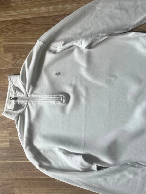 Vit halvzip från Ralph Lauren - Snygg vit tröja med halv dragkedja från Ralph Lauren. Klassisk broderad logga på bröstet i grått och hög krage. Tillverkad i mjukt bomullsmaterial och har långa ärmar. Perfekt för en clean och stilren look.