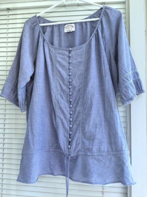 Blå loose-fit blus med knappar - Blå blus med knappar framtill och knytband i nederkant från Hilfiger Denim.  Ärmarna är trekvartslånga med dekorativa sömmar. Blusen har en rundad halsringning. Storlek L. Från armhålan till armhålan 59cm, längd 67cm.  Vissa ställe lite noppig, men inte märkbar(sista bild) 100% bommul.