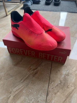 Puma Future 7 play it - Sunset Glow - Säljer ett par snygga fotbollsskor från Puma i en intensiv röd färg med svarta detaljer och logga på sidan. Skorna har en strömlinjeformad design och ovandel i syntetmaterial för bra bollkontroll. Perfekta för dig som vill sticka ut på planen.