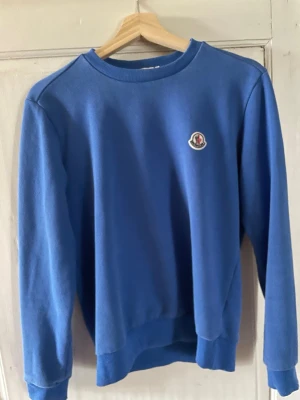 Blå sweatshirt från Moncler - En stilren blå sweatshirt från Moncler med rund halsringning och Moncler-logga på bröstet. Tröjan har ribbade muddar vid ärmslut och nederkant. Perfekt för en avslappnad och trendig look.
