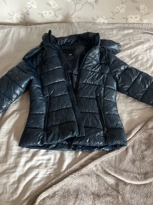 Mörkblå pufferjacka  - Snygg mörkblå pufferjacka från lager 157 med huva och dragkedja framtill. Jackan har quiltad design och två sidofickor med dragkedja. Perfekt för kalla vinterdagar och ger en cool look.