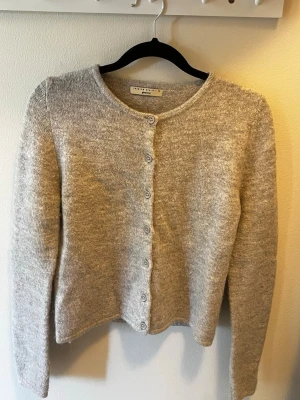 Grå kofta från Gina tricot  - Mysig grå kofta från Gina tricot med knäppning framtill. Koftan har lång ärm och är stickad i ett mjukt material. Enkel och stilren design som passar till många olika outfits.