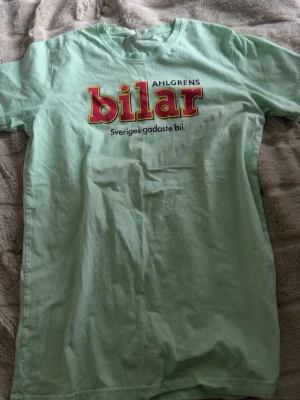 Ahlgrens bilar mintgrön t-shirt - Mintgrön t-shirt med tryck från Ahlgrens bilar och texten 'Sveriges godaste bil' på bröstet. Klassisk rund halsringning och korta ärmar. Perfekt för dig som gillar godis och vill ha en unik och rolig t-shirt i garderoben.