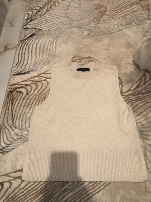Beige stickad väst med slits - Säljer en stilren beige stickad väst med ribbad kant nedtill och små slitsar i sidorna. Perfekt att bära över en skjorta eller t-shirt för en trendig lager-på-lager-look. Enkel och clean design utan mönster. Är öppen med prisförslag😊