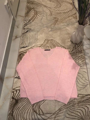 Ljusrosa stickad tröja med v-ringning - Mjuk och ljusrosa stickad tröja från Lager 157 med v-ringad hals och långa ärmar. Tröjan har en avslappnad passform och ribbstickade muddar vid ärmslut och nederkant. Perfekt för att skapa en chill och trendig look. Använd endast ett fåtal gånger. Är öppen med prisförslag😊