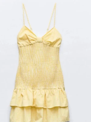 Gul kort sommarklänning med volang från Zara - Söt gul kort klänning med tunna axelband och volang nedtill. Klänningen har ett diskret randigt mönster och en feminin passform som framhäver midjan. Perfekt för varma dagar och somriga tillfällen. Väldig trendig! Skriv för fler bilder