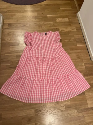 Rosa och vit rutig klänning Shein - Söt rosa och vit rutig klänning från Shein Curve med volangdetaljer och korta ärmar. Klänningen har en luftig passform och är tillverkad i ett lätt bomullsliknande material. Perfekt för varma dagar och ger en lekfull vibe.