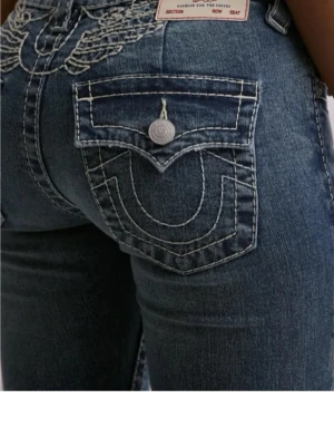 True Religion jeans med broderi - Snygga blå jeans från True Religion med broderade vingar vid fickorna. Knappt använda så i mycket bra skick bortsett från en slitning längst nere på ena benet,  skriv om ni vill ha bild på detta eller vid andra funderingar💖