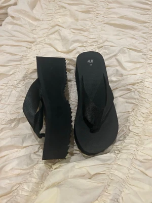 Svarta platåsandaler från H&M - Snygga svarta platåsandaler från H&M med breda remmar i textil och tjock sula i gummi. Perfekta flip-flops med modern chunky look och räfflad undersida för extra grepp. 