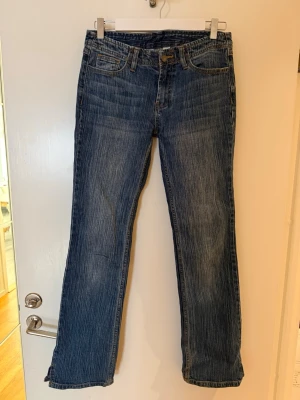 Blå bootcut jeans. Brandy Melville  - Säljer ett par klassiska blå bootcut jeans med snygga slitningar och kontrastsömmar. Jeansen har fem fickor, bälteshällor och dragkedja med knapp. Perfekta för en avslappnad och trendig look. Innerben 81 cm. Midja, från kant till kant 39 cm