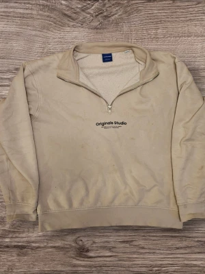 Beige half zip från Jack & Jones - Säljer en beige half zip sweatshirt från Jack & Jones Originals Studio. Tröjan har en hög krage med dragkedja och tryckt logga på bröstet. Insidan är mjuk och fleece-liknande, perfekt för chilliga dagar. Enkel och clean stil som funkar till det mesta.