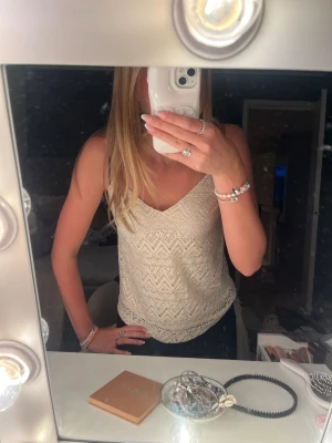 Vit spetsig linnetopp med v-ringning - Säljer en söt vit linnetopp med v-ringning och tunna axelband. Toppen har ett spetsliknande mönster i zigzag och är perfekt för varma dagar. Passformen är normal och toppen är ärmlös för en luftig känsla.