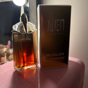 Alien Goddess Intense parfym Mugler - Alien Goddess Eau de Parfum Intense från Mugler i en lyxig, bärnstensfärgad glasflaska med futuristisk design och silvriga detaljer. Parfymen kommer i originalkartong och har en unik, elegant look som verkligen sticker ut på hyllan.
