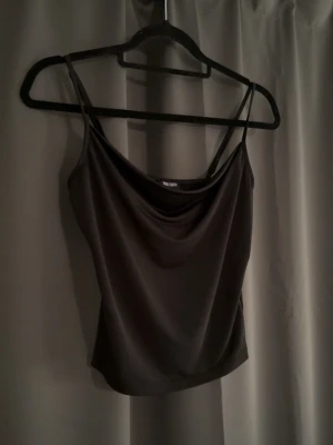 Svart linnetopp  - Snygg svart linnetopp med smala axelband och draperad urringning. Toppen har en croppad passform och är tillverkad i ett mjukt, glansigt material som ger en lyxig känsla. Perfekt att styla med jeans eller kjol.