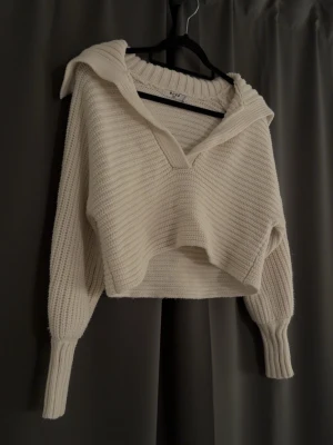 Vit stickad croppad tröja med krage - Säljer en vit stickad croppad tröja från NAKD med bred krage och v-ringning. Tröjan har långa ärmar med breda muddar och är gjord i ett mjukt, ribbstickat material. Perfekt för lager-på-lager och chill stil.