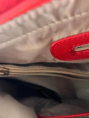 Rödvit randig handväska Michael Kors - Snygg handväska från Michael Kors med breda röda och vita ränder. Väskan har guldfärgad logotyp, röda handtag med dekorativt MK-hänge och dragkedja på insidan. Tillverkad i tåligt konstläder med textilfoder. Enda negativa är att dragkedjan till mittenfalet är trasigt annars väldigt bra skick 