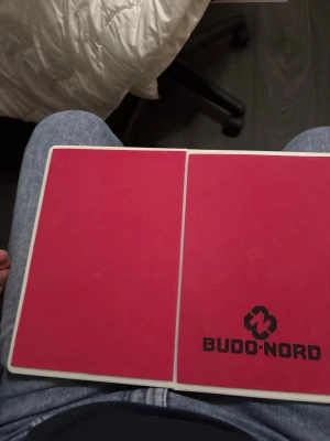 Röd brytbräda från Budo-Nord - Brytbräda från Budo-Nord i röd färg med vit ram. Brädan är rektangulär och har en tydlig logga på ena sidan. Perfekt för kampsportsträning och övningar där man tränar slag- och sparkteknik. Denna är den näst sista/starkaste brädan