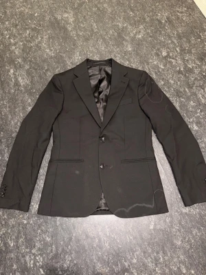 Kostym från Dressmann - Stilren hel kostym från Dressmann. Har använd den bara 1 gång. Kommer med byxorna också. Den vita T-Shirt får du grattis med köpet. Storlek ser du på bilden. Inga hål eller dåliga märke på den. Priset kan diskuteras.