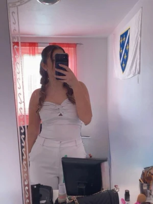 Vit bandeau tubtopp med twistdetalj - Säljer en snygg vit bandeau tubtopp med twistad detalj framtill och liten cut-out. Toppen är ärmlös och har en croppad passform som passar perfekt till höga byxor. Perfekt för dig som gillar stilrena och trendiga plagg. Använd 1 gång. Väldigt stretchig, passar folk som bär på strl S-M-L. Ordinarie pris 400kr. 