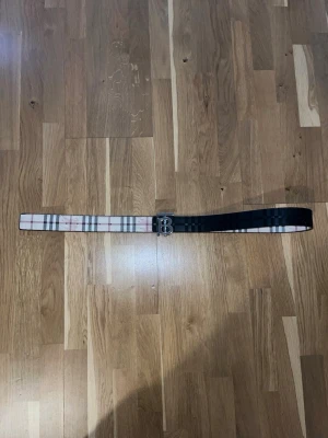 Burberry bälte - Reversibelt - Säljer ett elegant och stilrent Burberry bälte i fint skick. Bältet är Reversibelt, vilket betyder att du kan välja mellan två olika sidor för att matcha din outfit: det klassiska Burberry-mönstret och en stilren svart sida. Perfekt för att lyfta vilken look som helst!