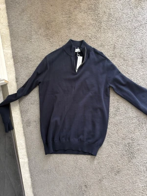 Mörkblå halv zip från John Henric  - Snygg mörkblå stickad tröja från John Henric Sweden i storlek M. Tröjan har halvzip i halsen, långa ärmar och ribbade muddar vid ärmslut och nederkant. Perfekt för lager på lager och enkel att matcha med jeans eller chinos.