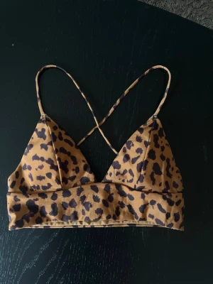 Leopardmönstrad bikiniöverdel - Bikiniöverdel med leopardmönster och tunna axelband som korsas i ryggen. Triangelformade kupor och bred resår under bysten.