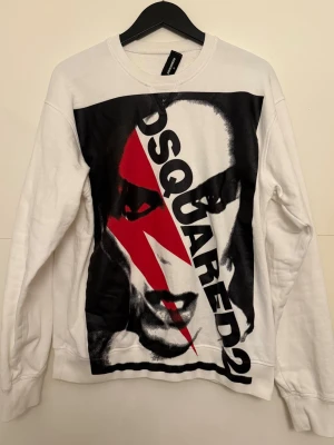 Vit sweatshirt från Dsquared2 - Cool vit sweatshirt från Dsquared2 med stort grafiskt tryck framtill i svart och rött. Tröjan har rund halsringning och långa ärmar. Perfekt statement-plagg för dig som gillar streetwear och unika prints. Storlek M, lös lapp på nacken. 