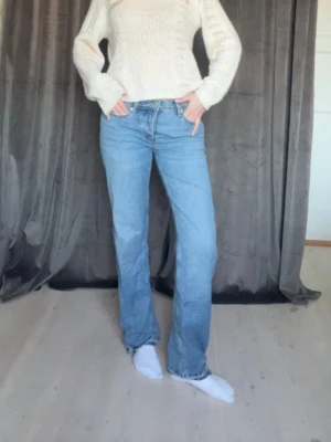 Ljusblå raka jeans med hög midja - Säljer ett par ljusblå jeans med rak passform och hög midja. Jeansen har klassisk femficksdesign och stängs med dragkedja och knapp. Perfekta för en avslappnad och trendig look. Materialet är denim i bomull. Dom är insydda i midjan och på sidan. Även nerlagda där nere